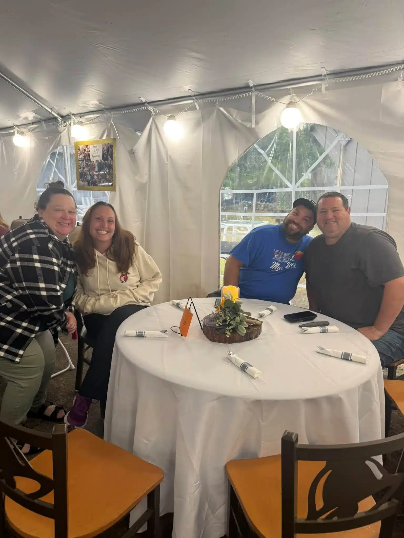 Four adults smiling around a decorated dining table beside an arched tent window at Acorn Acres Campground, Bozrah CT