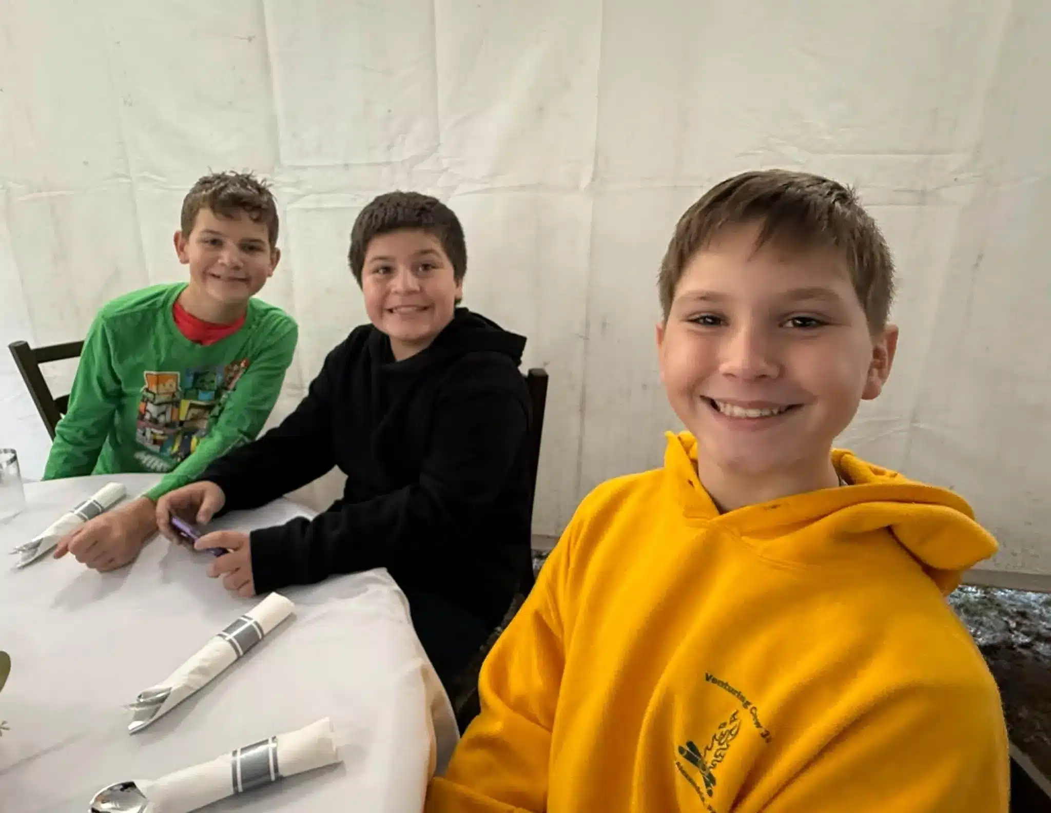 Three boys smiling together inside a white tent during a gathering at Acorn Acres Campground in Bozrah, CT