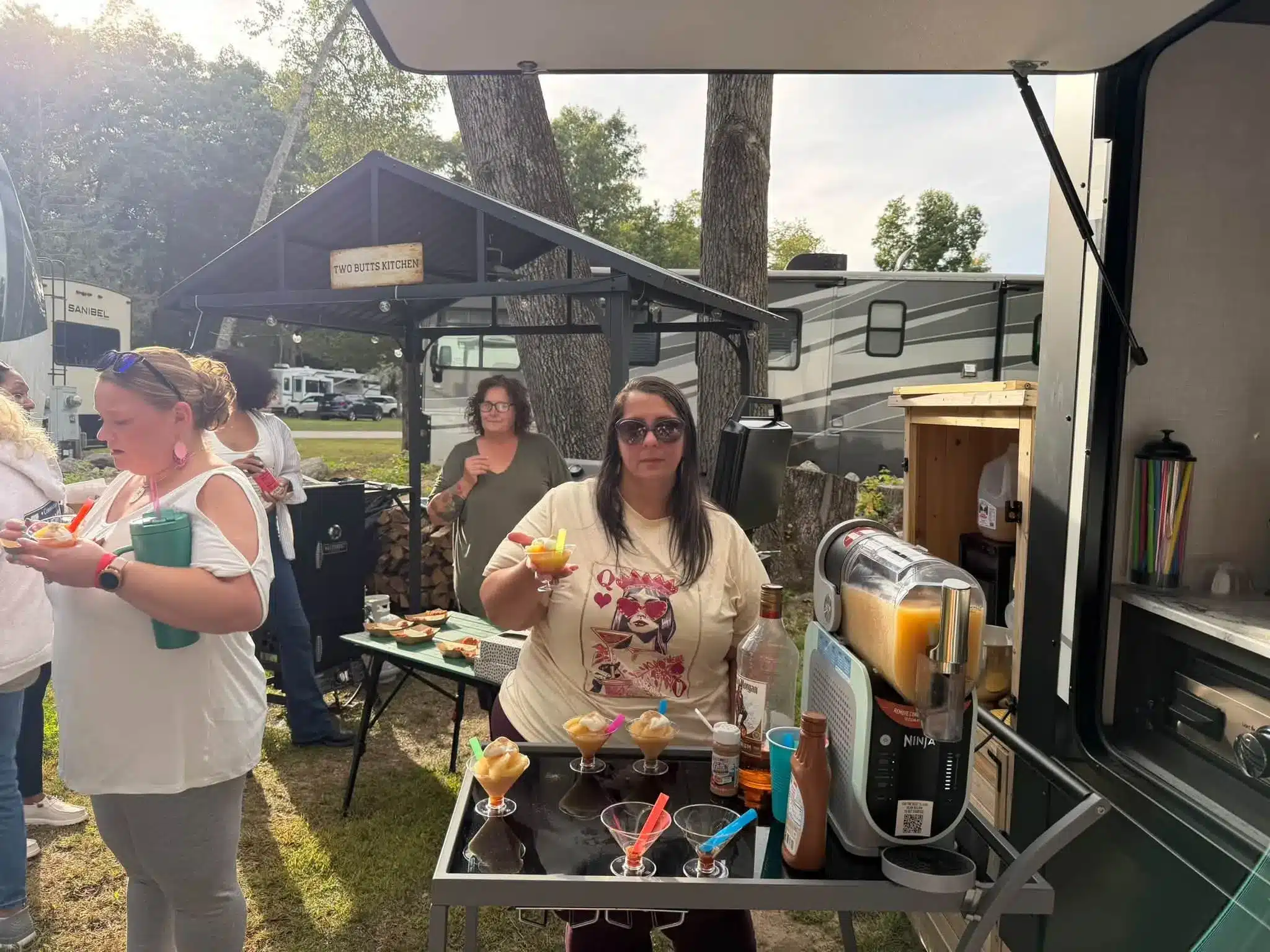 Women gathered at an outdoor counter and RV in the background at Acorn Acres Campground, Bozrah CT