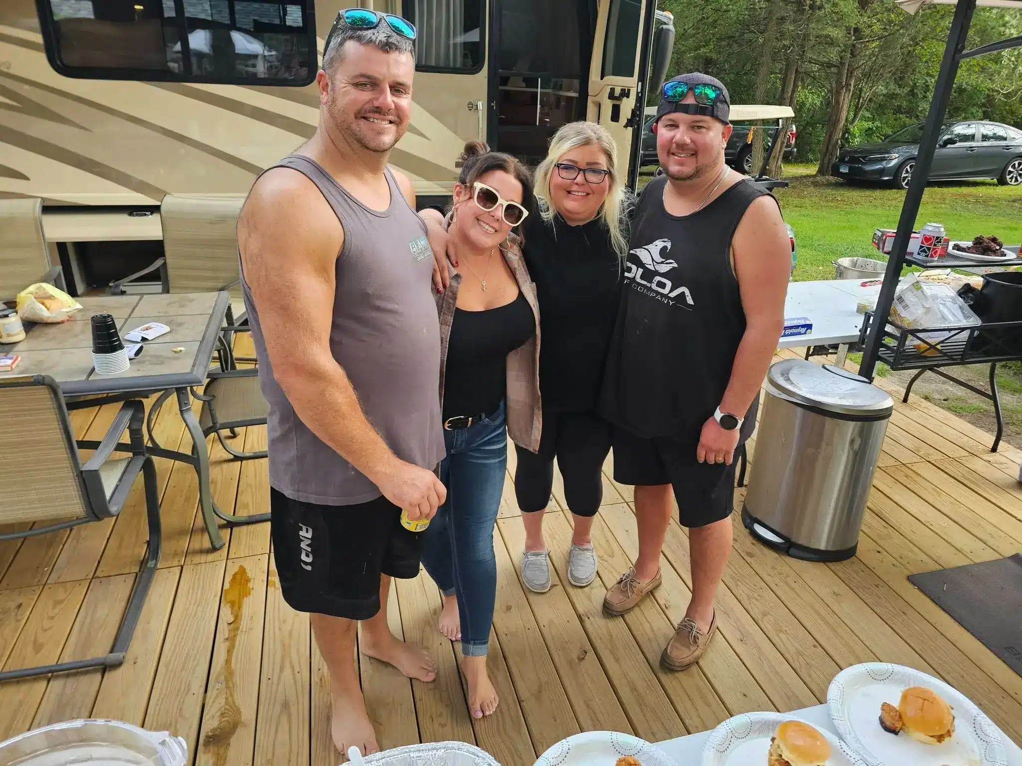 Four adults smiling together beside a travel trailer at an RV campsite at Acorn Acres Campground in Bozrah, CT